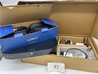 View of DVR unit along with two bundles of black cables in original Lorex box. Showing main DVR device with front panel buttons and LED indicators.