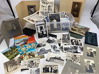 Overview of the collection displaying assortment of black and white photos, postcards, and mounted portraits spread out with some stacked in a plastic bin