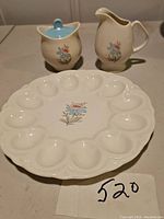 Set of three items: deviled egg dish, creamer, and lidded sugar bowl all with matching floral decals on ivory ceramic.
