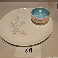 Chip and dip oval plate with small round bowl placed on top, showing floral decoration on plate and interior light blue of bowl.