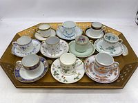 Top-down view of 10 assorted collectible teacups and matching saucers on gold-tone painted metal tray with lattice sides.