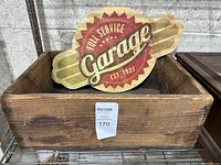 Wooden box containing the vintage-style garage sign, shows wood texture and dust accumulation.