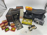 Wide view of the lot showing Kodak Autographic Junior, camera filters, Vivitar lens box, Tasco opera glasses in box, and Kodak Instamatic camera with case.