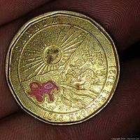 Reverse side of the coin depicting 1896 Klondike scene with sun, deer, maple leaves, text and red maple leaf symbol.