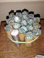 Top and bottom view of wrapped bank rolls of nickels with some loose coins in a plastic tube bundled with rubber bands.