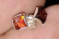 Close-up image of one amber stud earring held between fingers showing the orange translucent amber stone and silver setting.