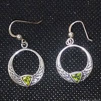 Photo showing the front view of the earrings on a black fabric background highlighting circular shape, gemstone, and silver engraving details.