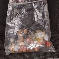 Clear plastic bag filled with a variety of polished mixed gemstones including agates and other stones, colors include white, orange, red, and yellow.