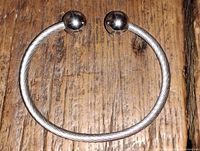 Stainless steel cable bracelet laid flat on a wooden surface showing the flexible cable construction and the two polished metal balls at each end.