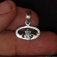 Front close-up view of the Irish Claddagh pendant held between fingers, showing detailed crown, heart, and hands design.