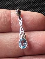 Close-up of sterling silver Celtic design pendant held between fingers showing light blue oval cut aquamarine gemstone and detailed silverwork.