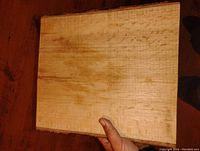 Photo of the rectangular chopping block showing the wood grain pattern and thickness, held by one hand to show scale