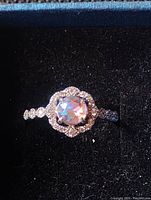 Front view of silver-tone ring with multi-color mystic topaz center stone surrounded by clear stones in a floral halo on a textured band.