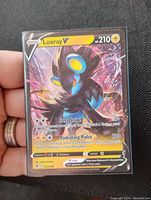 Photo showing the front of the Luxray V Holo Foil Pokemon card held in hand, highlighting the holographic effects, text details, and overall condition.