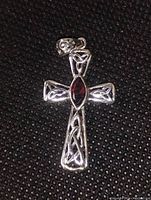 Front view of silver cross pendant with marquis cut red garnet center on black background