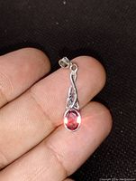 Close-up of hand holding pendant showing garnet stone and silver twisted design