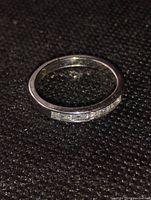 Silver women's ring with baguette cut stones channel set around the top half, shown on a black textured background.