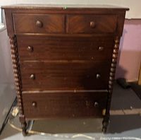 Full front view of the antique wooden dresser showing drawers, knobs, and spindled legs.
