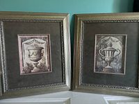 Two framed classical urn art prints side by side on wall