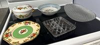 Six assorted serving dishes displayed on a stove top including porcelain, glass, and ceramic pieces