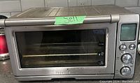 Front view of the Breville Smart Oven Pro showing stainless steel finish, glass window, and function buttons on the right side. Oven has a green tape label that says 'Sell'