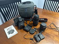 Overview of DSLR camera with attached kit lens, telephoto lens, battery charger, strap, manual and carrying case