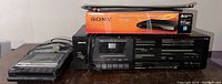 Panasonic cassette player, Nikko cassette stereo, and Sony DVD player in box on a wooden surface