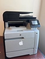 Front view of the HP laser printer showing Apple logo sticker on paper tray and touchscreen control panel.