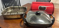 Kenmore electric fry pan with glass lid and power cord inside, stainless steel roaster, and red bread box on table.