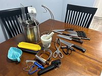 Full overview of kitchen utensils including cutting knives, utensil bin, banana holder, peelers, pastry blenders, and corn plates on table