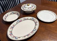 Four pieces on wooden table: covered serving bowl, large platter, small bowl, and dinner plate