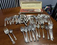 Overview photo showing assorted silver-plated flatware including forks, spoons, knives, piled on table with boxed Gorham serving fork and spoon on top.