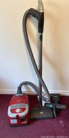 Full view of the Miele vacuum with hose, wand, and floor nozzle on carpeted floor.