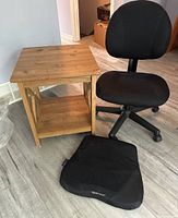 Black office chair, wooden side table and Obusforme cushion grouped on floor, showing overall condition and details.