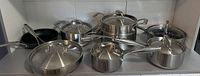 Front view of all 7 items including 5 stainless steel pots with lids, and 2 MSMK fry pans visually identified by black non-stick interiors.