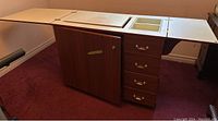 Wooden sewing table with folding extra leaves, cabinet, and drawer section visible.