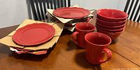 Full view of red stoneware plates, bowls and mugs stacked on table with some cardboard separators visible, showing quantity and condition.