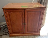 Front view of the rectangular wooden cabinet with two paneled doors and brass knob handles, medium wood finish.