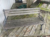 Full view of garden bench showing wooden slatted seat and backrest with cast iron ends on a wooden deck.