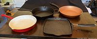 Four frying pans arranged on table showing different materials and sizes.