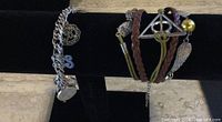 Two bracelets displayed on a black stand: one silver-tone charm bracelet and one multi-strand bracelet with mixed materials and charms.