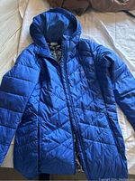 Full view of the blue long winter jacket laid flat showing front details and hood
