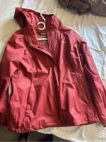 Front view of red Columbia rain jacket hanging on white hanger showing full zipper and hood.