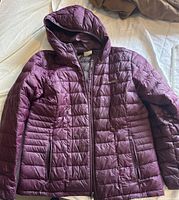 Front view of purple Columbia jacket with hood and zippered pockets on a bed.
