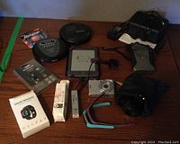 Photo of all items arranged on a table including electronic devices, chargers, smart bracelet box, camera, Kindle, disc players, flashlight, and watches.