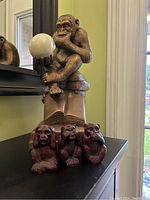 Four monkey figurines, three smaller Hear No Evil, See No Evil, Speak No Evil in dark cherry red and black, plus one larger Darwin thinking monkey sculpture with white orb on book base labeled Darwin.