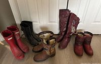 Five pairs of women's boots arranged on floor including rubber and winter styles.