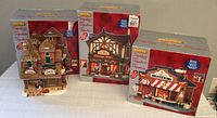 Three LEMAX Signature Collection Christmas village buildings in original boxes on display.