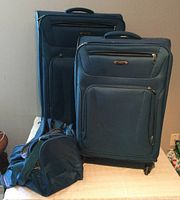 Set of two upright suitcases and one duffel bag shown standing on table, displaying their shape, color, and features.