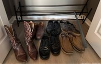 Photo showing brown leather cowboy boots size 13, three pairs of men's dress shoes in black and brown leather, two pairs of casual shoes, and the black metal shoe rack on floor.
